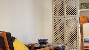 Una stanza con una sedia di legno, un tavolino con una ciotola, un paravento bianco con decorazioni a reticolo e un pavimento colorato in maiolica.