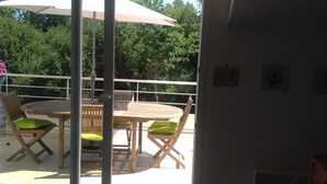 Ein Balkon mit Holztisch und -stühlen, einem weißen Sonnenschirm und Blick auf Bäume.