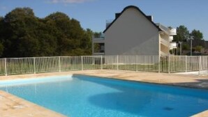 Ein rechteckiger Pool mit gefliestem Sonnendeck, umgeben von einem weißen Metallzaun.