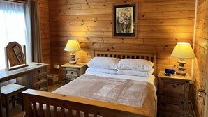 A wooden cabin room with a bed, two bedside tables with lamps, a desk, and a framed picture on the wall. - Cherry Lodge, Cedar Springs, Self Catering Log Cabin, Heacham,Close to the Beach (King's Lynn)