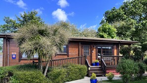 A wooden lodge with a porch, steps, and a gravel driveway. - Cherry Lodge, Cedar Springs, Self Catering Log Cabin, Heacham,Close to the Beach (King's Lynn)