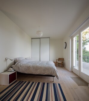 Quarto com cama, mesa de cabeceira, cadeira, janela e porta.