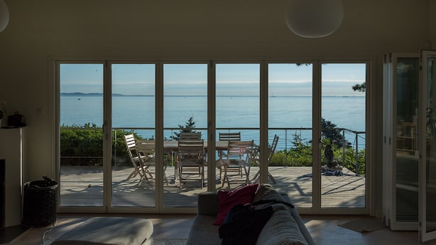 Ein Wohnzimmer mit einem großen Schiebeglasfenster, das auf eine Terrasse mit Blick aufs Meer führt.