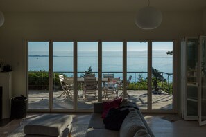 Un salon doté d’une grande porte-fenêtre coulissante donnant sur une terrasse extérieure avec vue sur la mer.