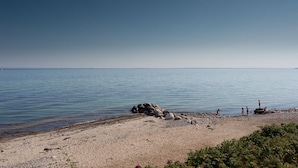 Ein Strand mit blauem Himmel, ruhigem Wasser und einigen Personen in der Nähe des Ufers.