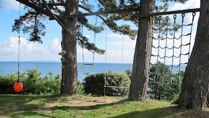 Ein Baumhaus mit einer Reckschaukel und einer Netzbrücke, mit Blick auf ein Gewässer.