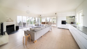 Ein geräumiges Wohnzimmer mit einer großen, grauen Couch, einem Kamin und einem Essbereich mit Tisch und Stühlen.