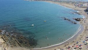 Una playa costera con aguas claras, costa rocosa y una zona de arena con sombrillas y gente.
