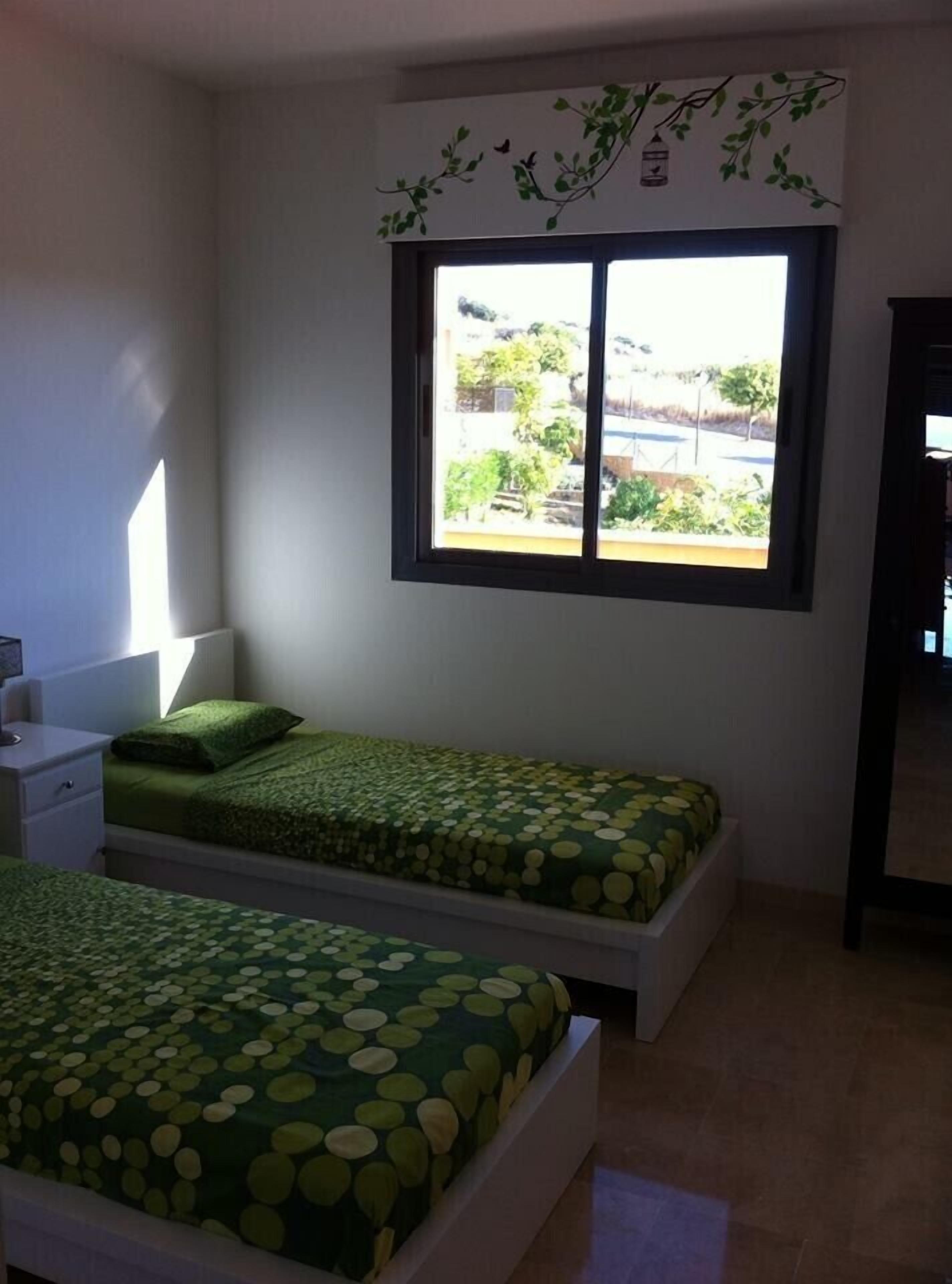 Une chambre avec deux lits simples, une table de chevet, une fenêtre donnant sur un espace verdoyant et un élément décoratif mural.