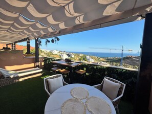 Un patio al aire libre con vistas al mar y grúas de construcción, que presenta una mesa redonda con individuales y sillas de mimbre.