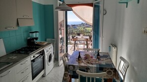 Une cuisine équipée d’un lave-linge, une table dressée avec une nappe et des bougies, et une vue sur un balcon avec des chaises et une table.