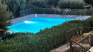 Une piscine rectangulaire entourée d’une clôture métallique, avec un escalier menant à l’espace piscine.