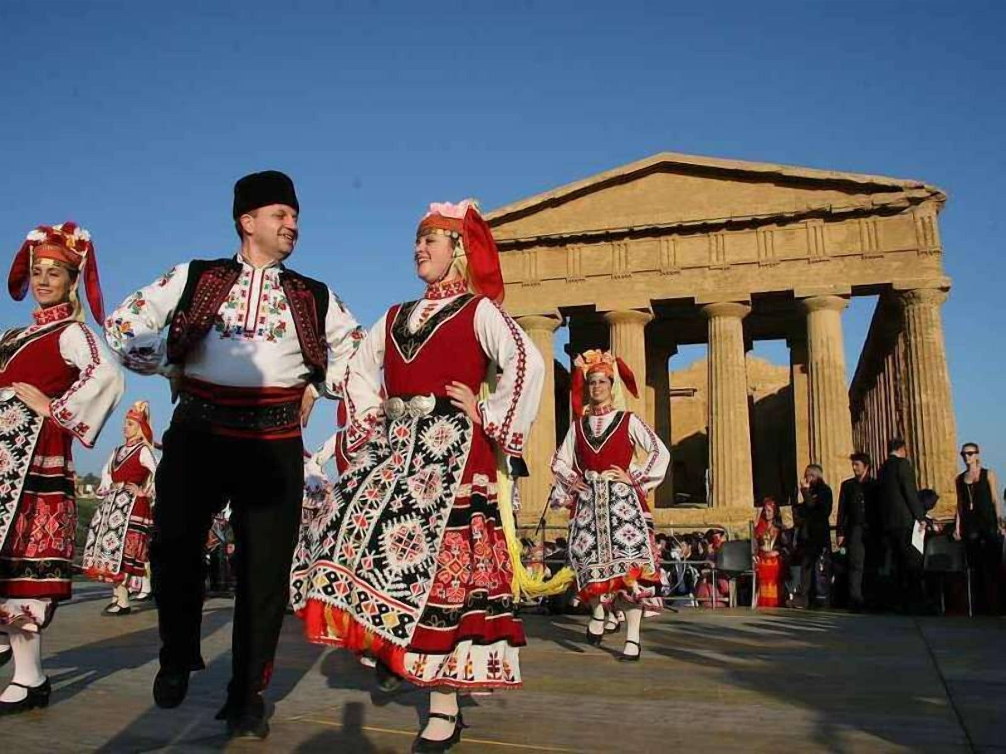 A group of people in traditional attire performing in front of a classical building with columns.