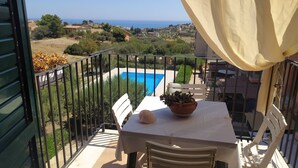 Un balcon donnant sur une piscine, une table avec un pot de fleurs et une chaise.