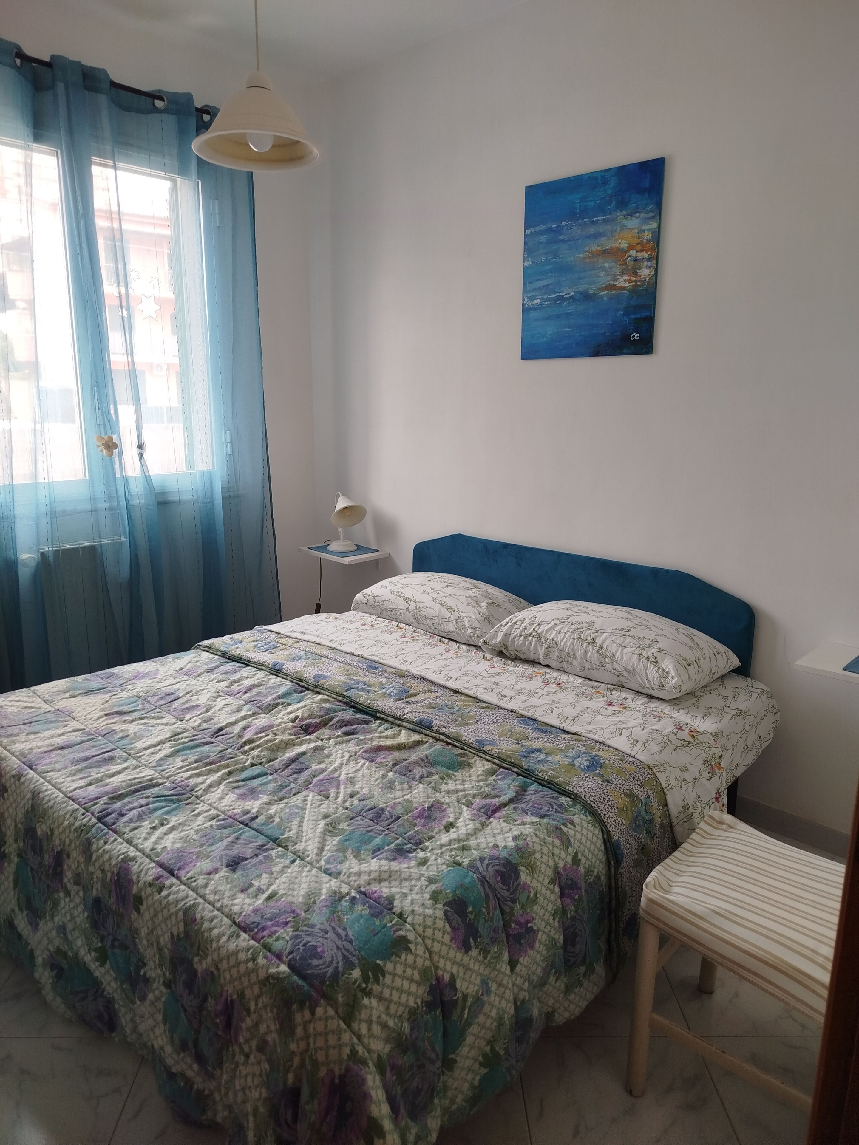 Une chambre à coucher avec un lit, une table de chevet, une chaise, une lampe suspendue et un tableau au mur.