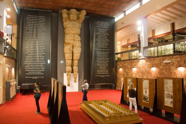 A museum interior with a large dinosaur skeleton, informational panels, and a model of a building.