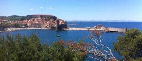 A coastal town with a prominent fort, a clear blue sky, and surrounding greenery.