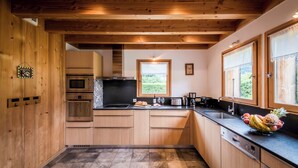 Een moderne keuken met houten kastjes, een inbouwoven, een magnetron en een groot raam met uitzicht op groen.