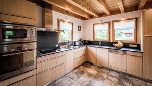 Een moderne keuken met houten kasten, roestvrijstalen apparatuur en grote ramen met uitzicht op de omgeving.