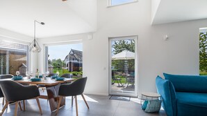 Un comedor moderno con una mesa de madera y sillas negras, un sofá azul y vistas al exterior a través de amplios ventanales.