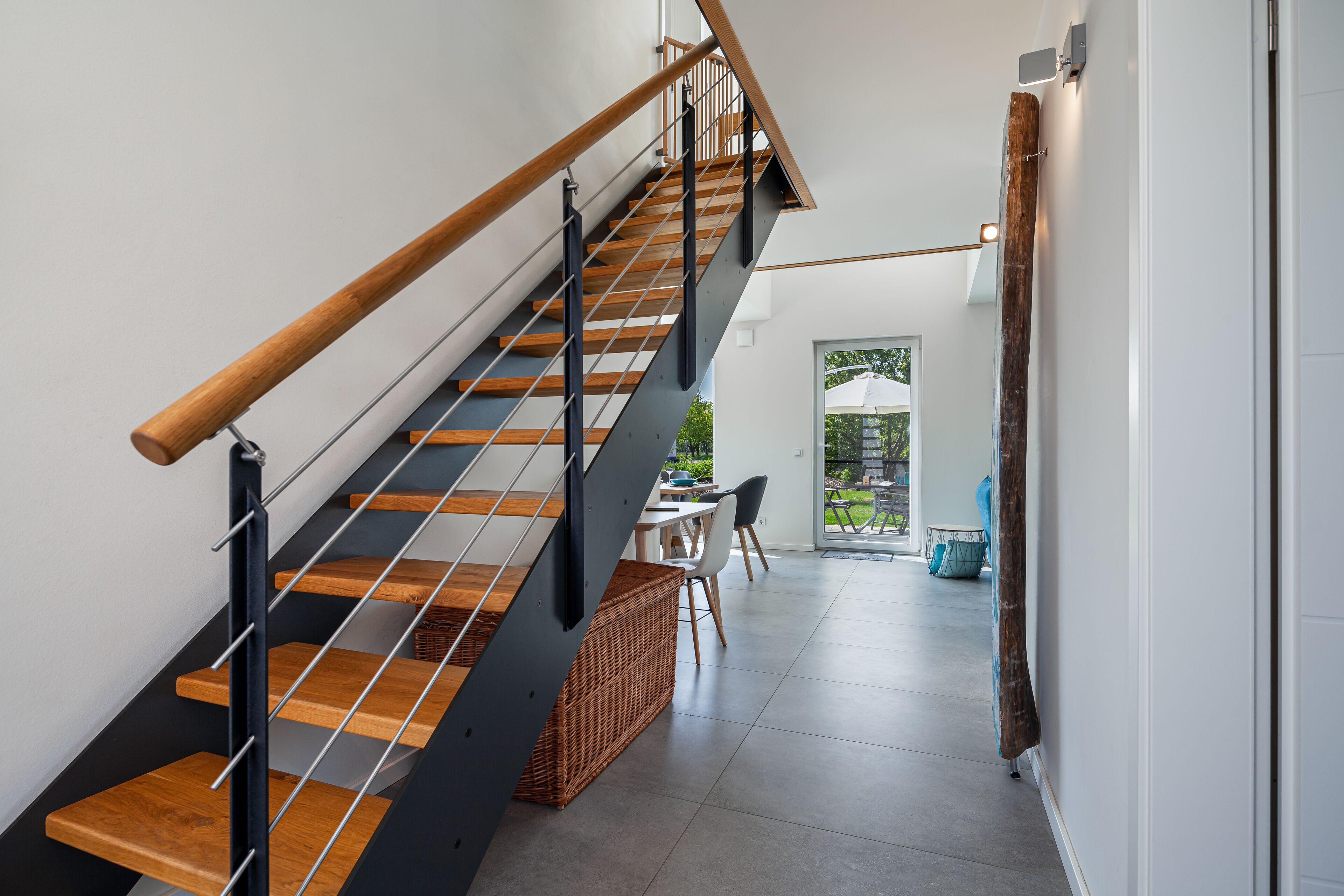 A modern staircase with wooden steps and metal railings, leading to a dining area with a table and chairs.