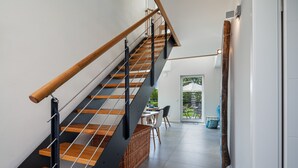 Una escalera moderna con escalones de madera y barandillas metálicas que conduce a un comedor con una mesa y sillas.