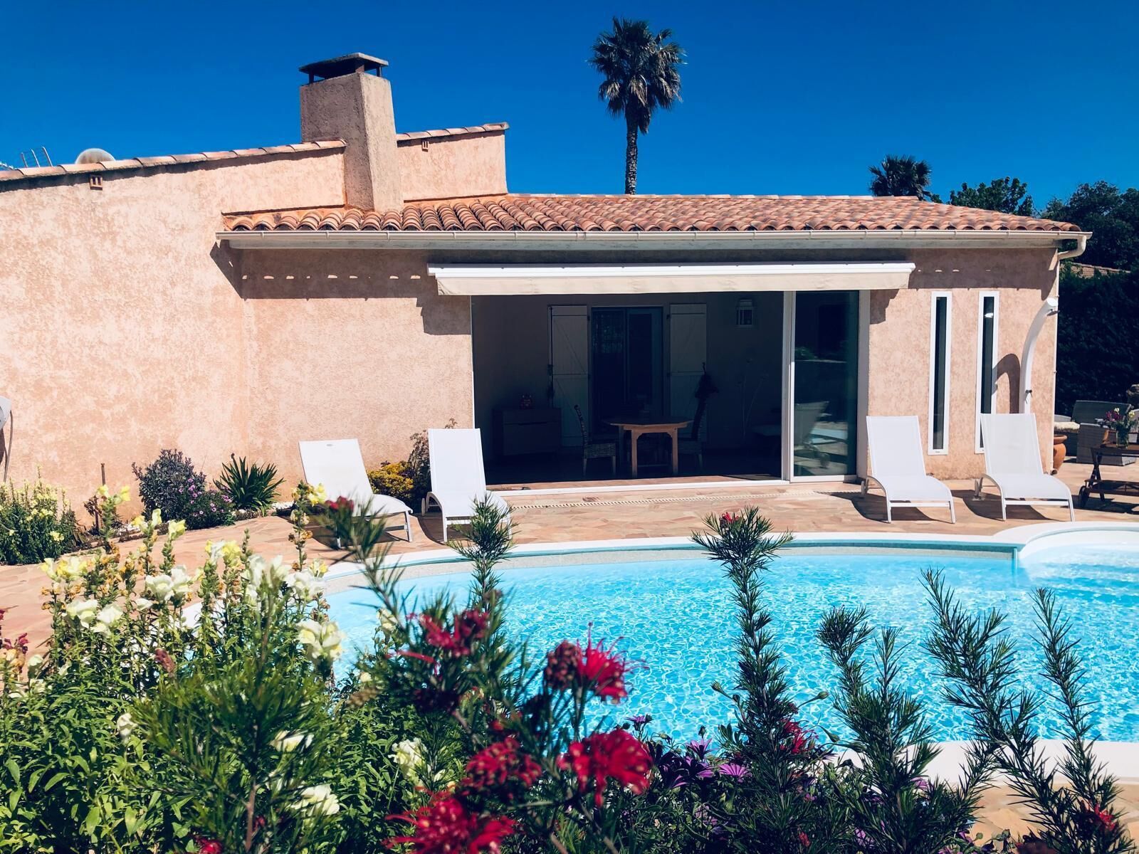 Una casa con piscina, sillas de descanso blancas y una zona de patio.