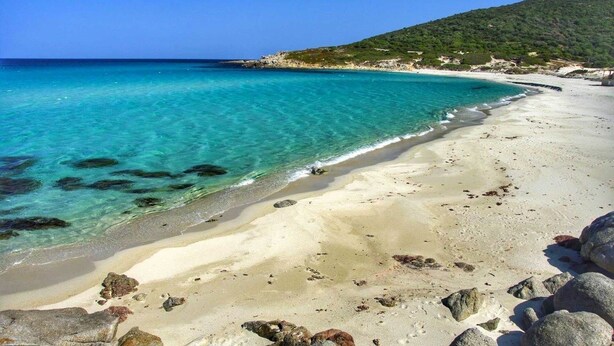 Una platja amb aigua turquesa cristal·lina, sorra daurada i roques al costat.