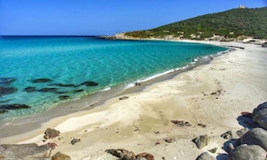 Uma praia com águas turquesa cristalinas, areal arenoso e formações rochosas.