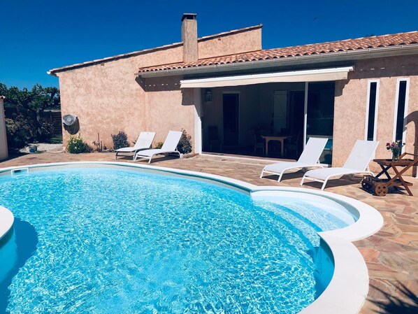 Une piscine avec des chaises longues, un patio couvert et un bâtiment doté d’un toit en tuiles.
