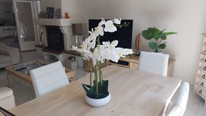 Una zona de dinar amb una taula de fusta, cadires blanques i un vas amb orquídies blanques.