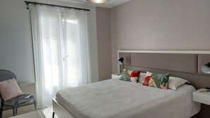 Une chambre à coucher avec un grand lit, une chaise, une table de chevet et une fenêtre ornée de rideaux légers.