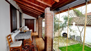 Um alpendre coberto com uma mesa de jantar, cadeiras e vista para um jardim e um edifício.