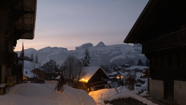 A snow-covered village with traditional wooden houses, a lit building in the foreground, and mountains in the background. - authentic luxury chalet with garden (La Forclaz)