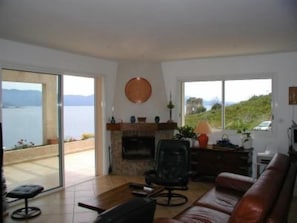 Un salon avec une cheminée, un canapé, un fauteuil et une vue sur la mer.