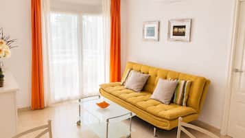 Una sala de estar con un sofá amarillo, una mesa de centro de vidrio y cortinas naranjas.