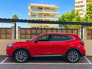 A red SUV parked in a covered parking area with a building in the background. - Apartment on the beachfront, front sea view, swimming pools, tennis (Calpe)