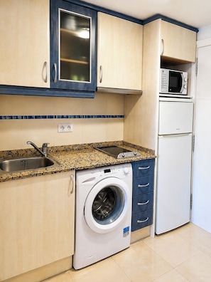 Uma cozinha compacta com máquina de lavar, micro-ondas e pia.