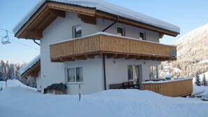 A two-story chalet with a wooden balcony, a ski lift in the background, and a snowy mountain landscape. - Luxury vacation home for summer with private pool and winter at the slopes (Annaberg)