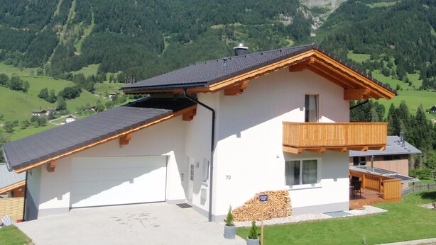 A two-story house with a balcony, a garage, and a mountain backdrop. - Luxury vacation home for summer with private pool and winter at the slopes (Annaberg)