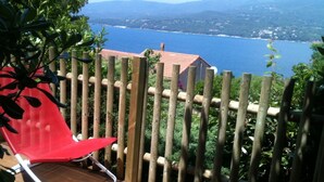 A wooden deck with a red chair, overlooking a body of water and distant mountains. - Apartment/ flat - PROPRIANO (Propriano)