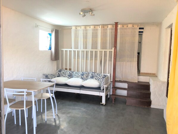 Ein Zimmer mit einer weißen Couch, einem Holztisch und Stühlen. Eine Treppe führt zu einer weiteren Ebene.
