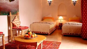 Una habitación de hotel acogedora con dos camas, una silla de madera, una mesa con fruta y apliques decorativos en la pared.
