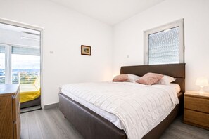 Ein Schlafzimmer mit Bett, Nachttischen, einem Fenster mit Jalousien und Blick ins Freie.