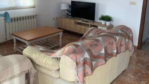 Un salon avec un canapé, une table basse en bois, un téléviseur et un lustre.