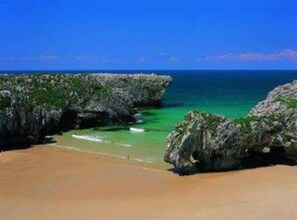 Una playa con aguas turquesas cristalinas, formaciones rocosas y una orilla arenosa.
