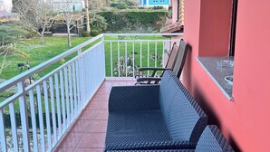 Un balcon avec un canapé en osier, une balustrade blanche et une vue sur un paysage verdoyant parsemé de maisons.
