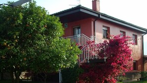 Une maison à l’extérieur rouge, avec un balcon blanc et un arbre aux feuilles vertes et aux oranges.