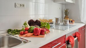 A kitchen with a white countertop, a stainless steel sink, and red cabinets. There are various vegetables and fruits on the counter, including tomatoes, carrots, and a pineapple. - Beautiful **** villa with heated pool, summer kitchen, WiFi, grill, fitness, 1.5 km from the sea (Pula)
