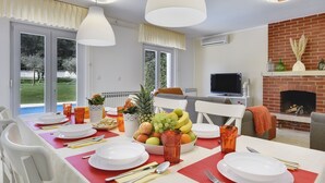 A dining area with a table set for four, a fruit bowl, and a fireplace. - Beautiful **** villa with heated pool, summer kitchen, WiFi, grill, fitness, 1.5 km from the sea (Pula)